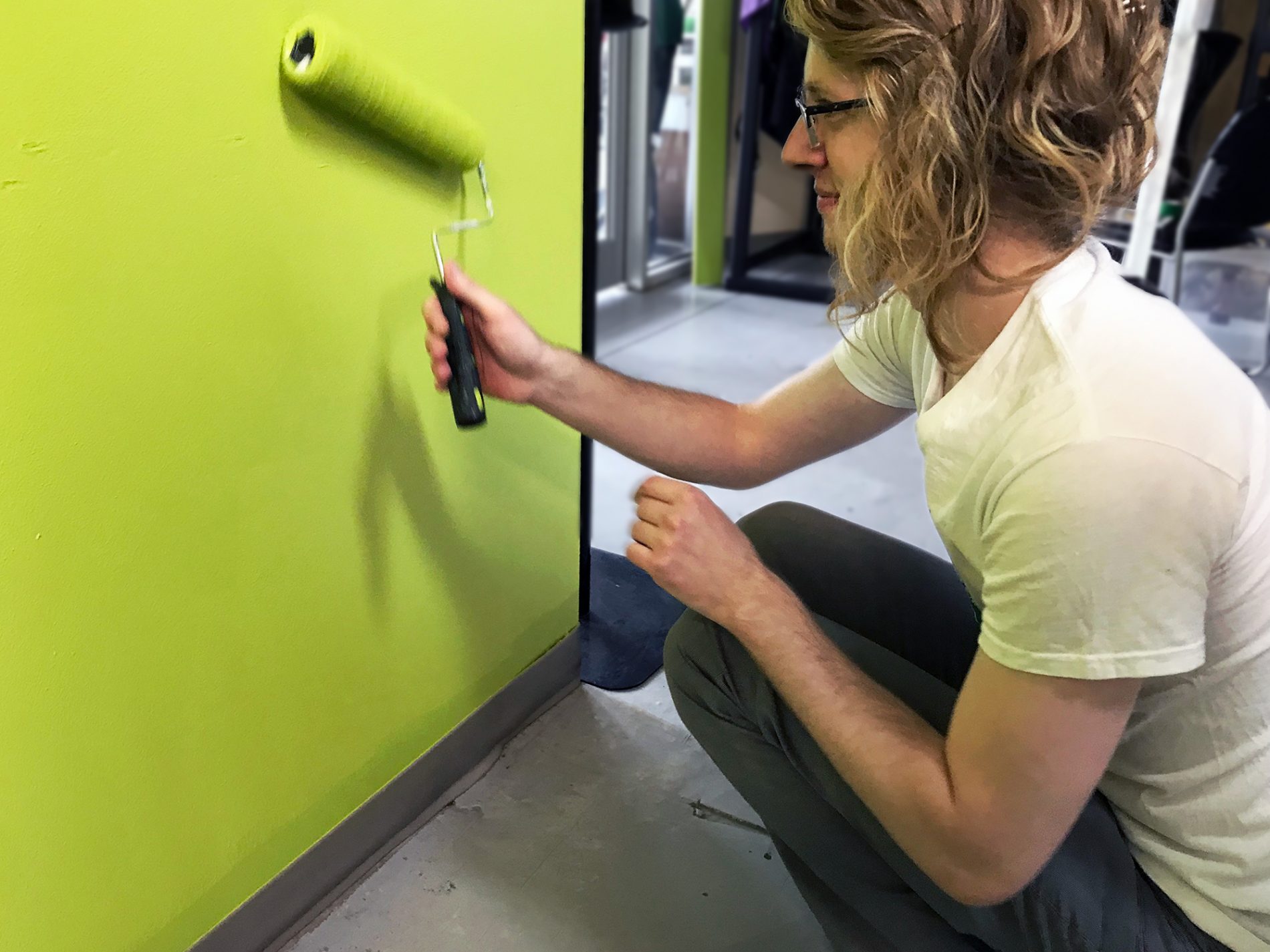 Mitch kneeling down painting a wall bright green with a paint roller