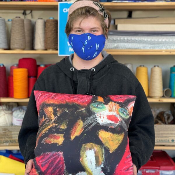 Ashley holding a square pillow with her cat drawing on it.