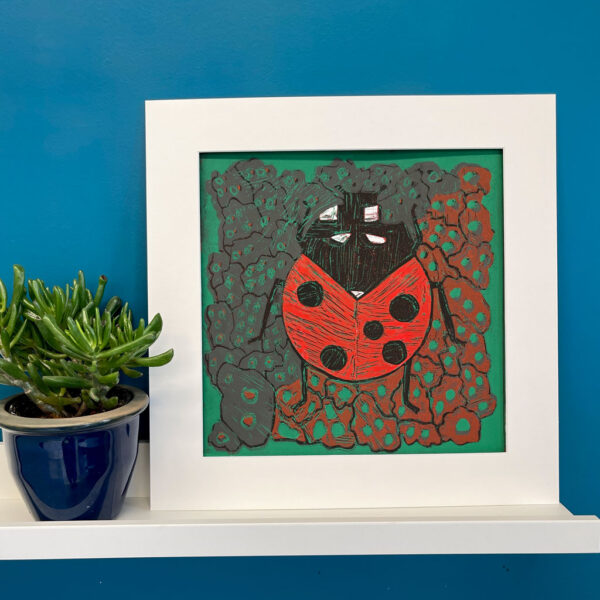 Lady Bug linocut in a white mat on a shelf