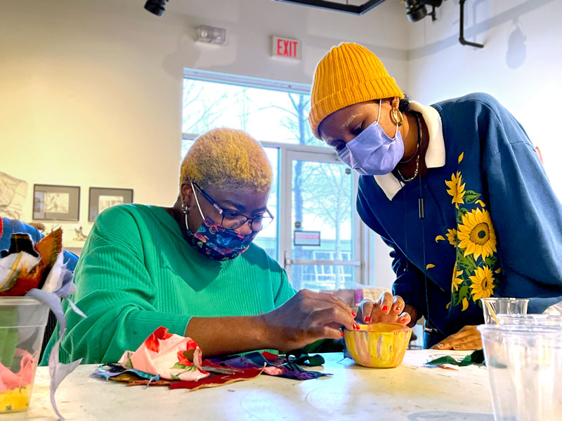 Aba and Raneece adding fabric to a small yellow pinch pot