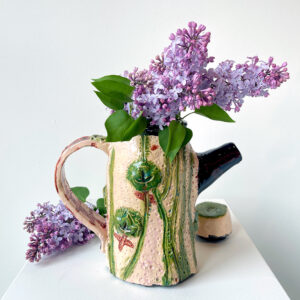 Beige teapot decorated with leaves and vines full of lilacs