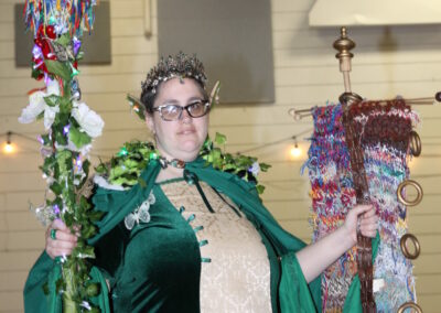 Bonnie wearing a green and gold dress with a cloak and staff