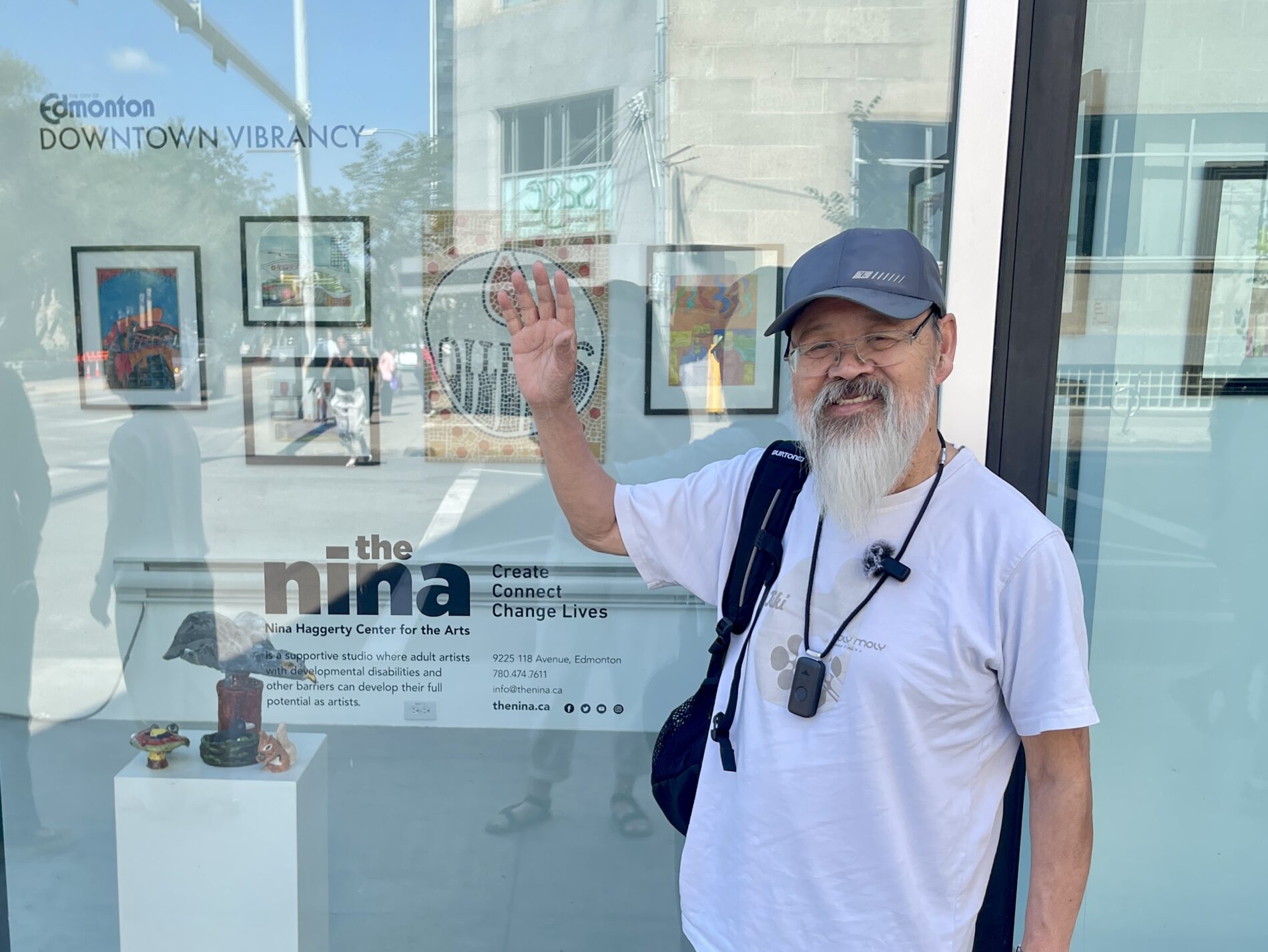 Raymond standing outside a window. Inside the window there are framed artworks on the wall and text that says "Downtown Vibrancy", with the Nina's logo.